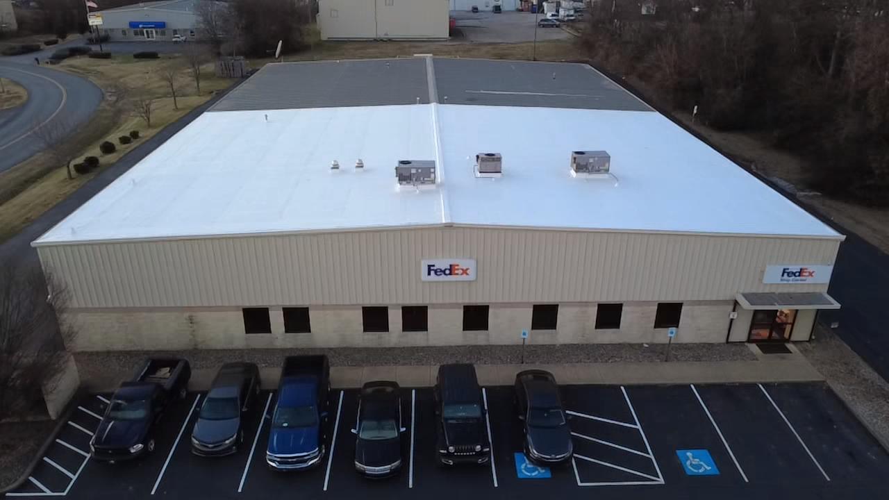 Aerial view of the FedEx Ship Center with new white membrane roofing installed over half of the old dark metal roof